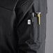 A person wearing a black Uncommon Chef long sleeve chef coat with a tool in the pocket.