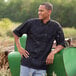 A man wearing a black Uncommon Chef Montego Pro Vent chef coat with a mesh back.