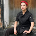 A woman in a black Uncommon Chef short sleeve chef coat sitting on a wooden door.