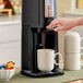 A person's hand pouring coffee into a white Zojirushi coffee pot on a table.