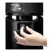 A hand pressing a button on a black Zojirushi beverage dispenser.