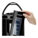 A hand holding a Zojirushi black thermal beverage dispenser with a glass lid.