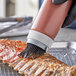 A person using a Tablecraft black silicone basting brush to brush sauce over a piece of meat.