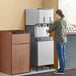 A woman using a Scotsman ice and water dispenser in a corporate office cafeteria.