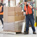 A man in a warehouse using a Lavex Aluminum Nelson wrapper on a pallet of boxes.