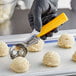 A person holding a yellow Choice #20 Thumb Press Disher filled with ice cream.