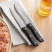 A plate of steak with a Choice jumbo steak knife and fork on a napkin.