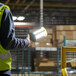 A person in a yellow vest holding a Lind Equipment Beacon360 LED portable hand lamp.