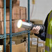 A person in a yellow vest holding a Lind Equipment Beacon360 LED hand lamp.