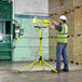 A man in a hard hat and safety vest adjusts a Lind Equipment LED dual head floodlight on a yellow tripod.