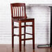 A Lancaster Table & Seating mahogany wood school house bar stool on a table in a restaurant.