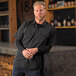 A man in a Mercer Culinary black short sleeve work shirt leaning on a brewery counter.