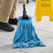 A person using a Lavex blue microfiber strip mop to clean a floor.