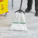 A person using a Lavex white microfiber wet mop with a 1" headband to clean a floor.