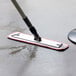 A Lavex red and white microfiber mop pad with hook and loop being used to clean a concrete floor in a professional kitchen.