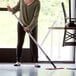 A woman using a Lavex red aluminum spray mop handle to clean a table.