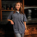 A woman standing in front of a counter wearing a grey Mercer Culinary short sleeve work shirt.