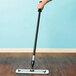 A hand uses a Lavex blue microfiber mop pad on a wooden floor.