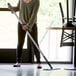 A woman using a Lavex blue aluminum spray mop handle to clean the floor.