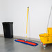 A black rectangular mop bucket with a yellow lid on the floor with a Lavex 36" Microfiber Pocket Dust Mop pad in it.