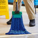 A person with a Lavex blue microfiber looped end wet mop cleaning the floor.