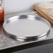 An American Metalcraft aluminum pizza pan on a metal counter.
