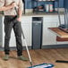 A man using a Lavex telescoping mop handle to clean a floor in a professional kitchen.