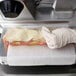 A person in gloves using a Globe meat slicer to cut ham for a sandwich.