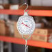 A round analog industrial hanging scale with a hook at the top and bottom for weighing items.
