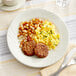 An Acopa ivory stoneware plate with a breakfast of eggs, sausage, and potatoes.