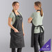 Two women wearing black cat denim aprons with black webbing.