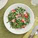 An Acopa ivory stoneware plate with a salad of strawberries, greens, and pine nuts on it with a silver knife and fork on a yellow cloth.