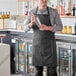 A black and white chalk stripe poly-cotton butcher bib apron with two pockets, worn by a person in a bar setting.
