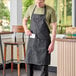 A man wearing a Uncommon Chef butcher apron with a pinstripe design in a professional kitchen.