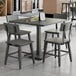 A square slate gray solid wood table with a live edge and four matching industrial-style chairs.