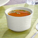 An Acopa ivory stoneware bouillon cup filled with soup on a table with a place mat