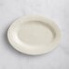 An Acopa ivory stoneware oval platter with an embossed design on the rim on a marble surface.