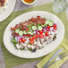 An Acopa ivory stoneware oval platter with salad, meat, and a side dish on it.