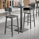 A Lancaster Table and Seating industrial bar height table with a live edge wood top and two bar stools with slate gray seats.