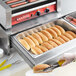 A person using an Avantco hot dog bun warmer to prepare a hot dog.