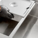 A person wearing black gloves using an Avantco stainless steel hotel pan adapter bar to hold a metal container.