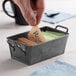 A person putting a packet of sugar into a black metal container.