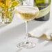 An Acopa Select coupe glass filled with champagne on a table with a bottle and flowers.