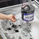 A hand using a Noble upright electric glass washer to clean a glass in a sink.