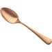 A close-up of a Bon Chef matte rose gold soup/dessert spoon with a handle.