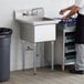 A man in a white shirt standing next to a Steelton stainless steel one compartment sink on a counter.