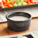 A glossy black Acopa fluted ramekin filled with white sauce on a table.