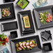 A table set with Acopa matte black square stoneware bowls filled with green soup.