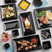 A table with black Acopa square stoneware plates of food.