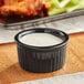 An Acopa glossy black fluted stoneware ramekin filled with white sauce.